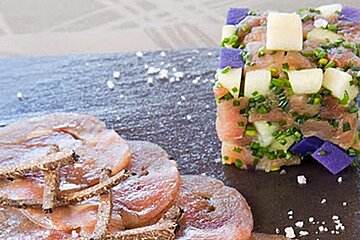 an image of a slate with sliced cold meats and a cube of vegetables on top